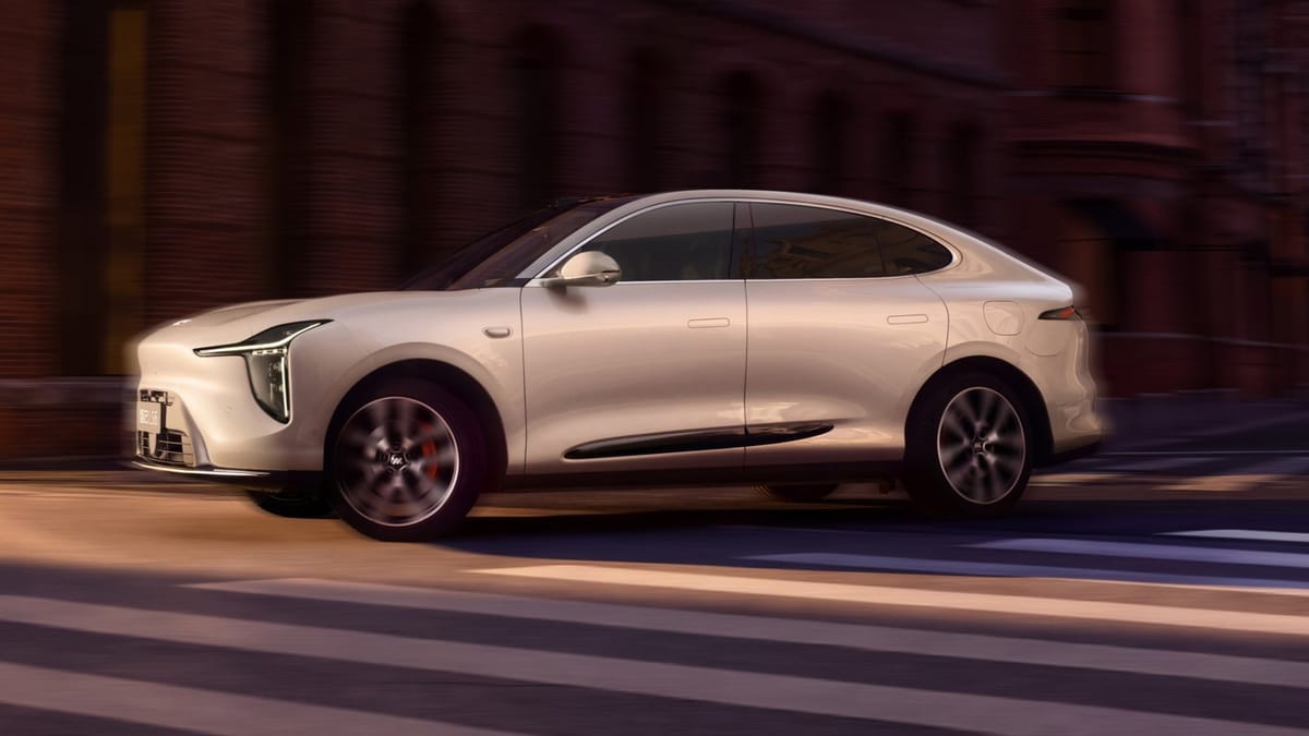 Weißes SUV-Coupé IM LS6 der neuen Generation fährt durch eine Straße mit Backsteinfassaden