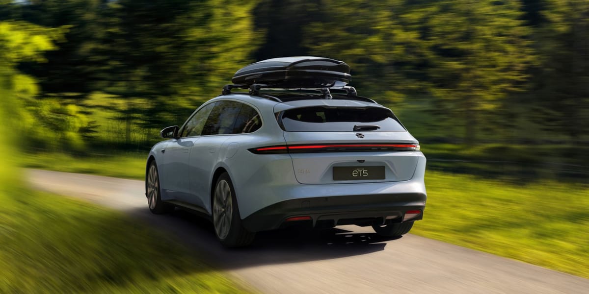 NIO ET5 Touring in Hellblau mit Dachbox fährt auf einer Landstraße durch den Wald