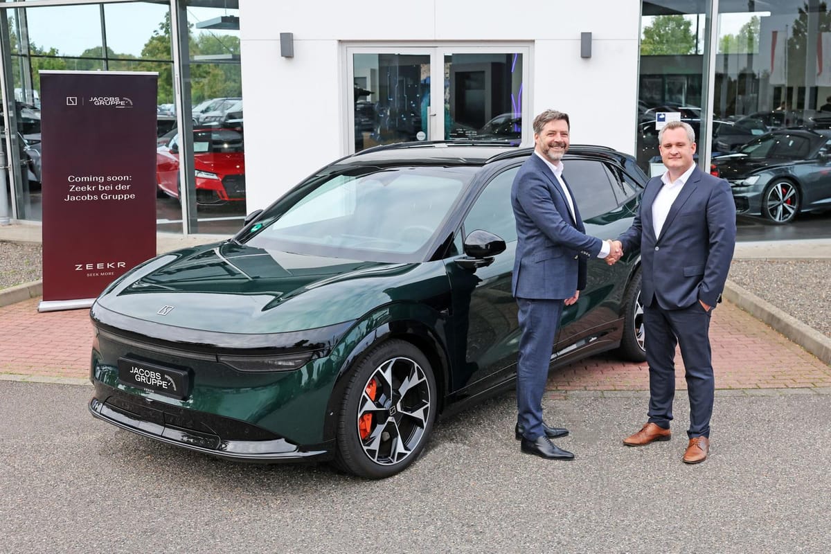 Handschlag zwischen Zeekr und der Jacobs-Gruppe vor einem dunkelgrünen Zeekr-SUV am Autohaus in Aachen