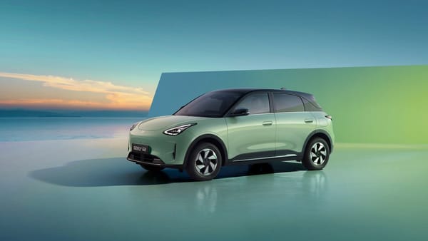 Ein mintgrüner Geely E2 steht vor einer blaugrünen Wand am Meer