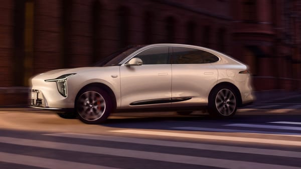Weißes SUV-Coupé IM LS6 der neuen Generation fährt durch eine Straße mit Backsteinfassaden