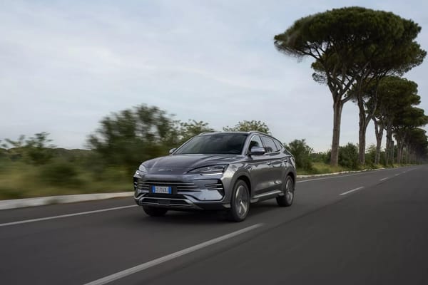 Grauer BYD Seal U DM-i fährt auf einer von Bäumen gesäumten Landstraße